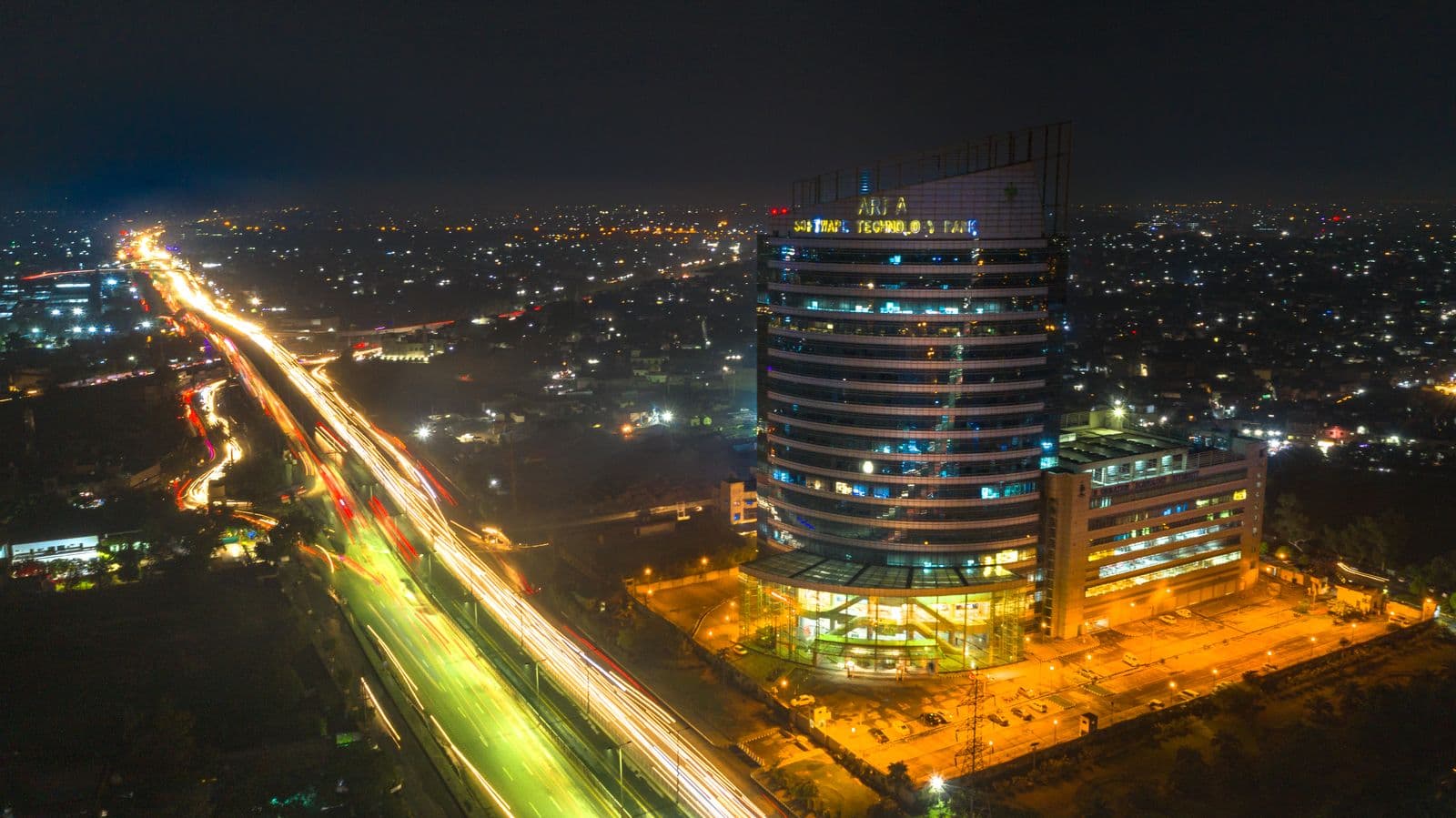 Light trails on a highway beneath a lit-up skyscraper in Lahore at night